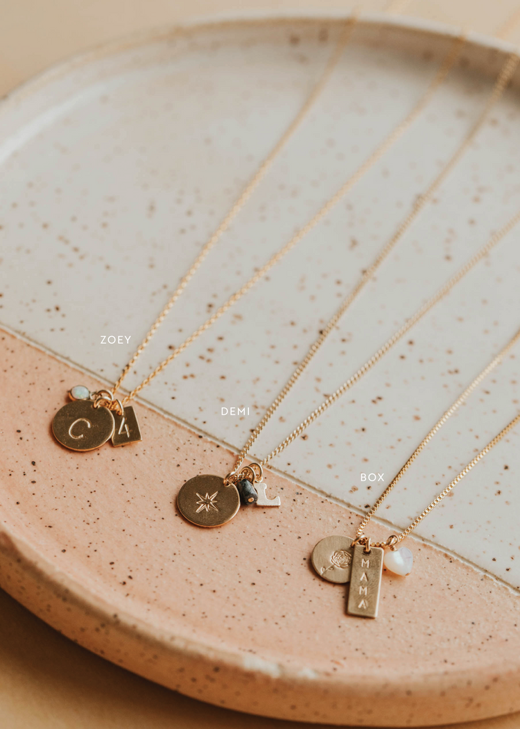 Gold necklaces with various pendants on a ceramic dish