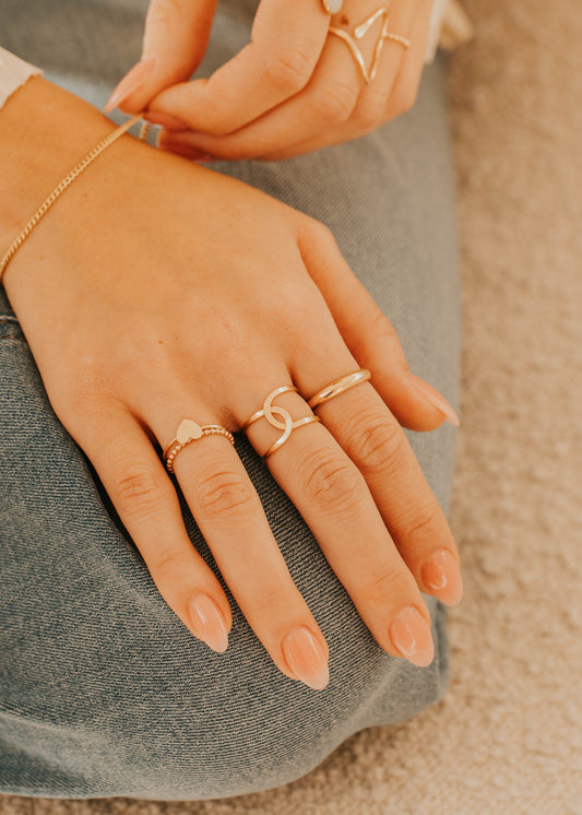 Close-up of hands wearing multiple gold rings on a neutral background