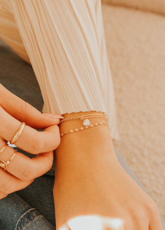 Close-up of a person's hand wearing multiple gold rings and a bracelet on a blurred background