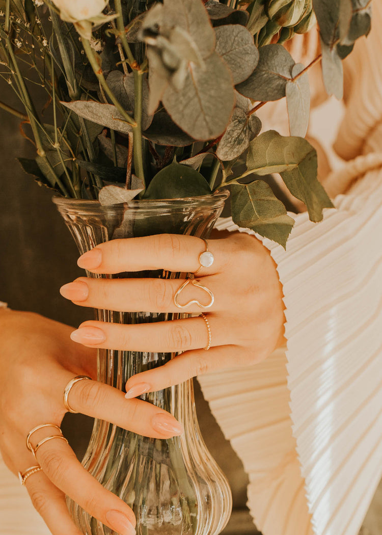 Person holding a clear vase with flowers, wearing a beige sweater.