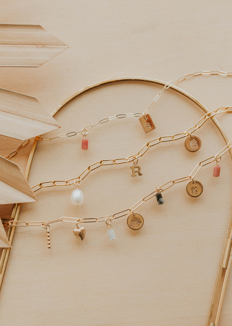 Gold chain with various charms on a beige background