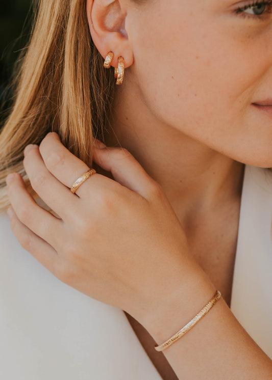 Close-up of a woman wearing gold jewelry including earrings, ring, and bracelet.
