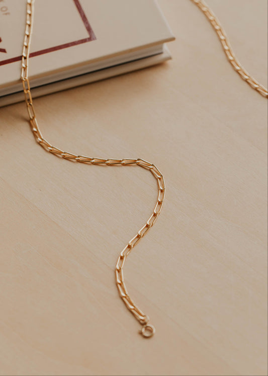 Gold chain necklace on a beige surface with a book in the background
