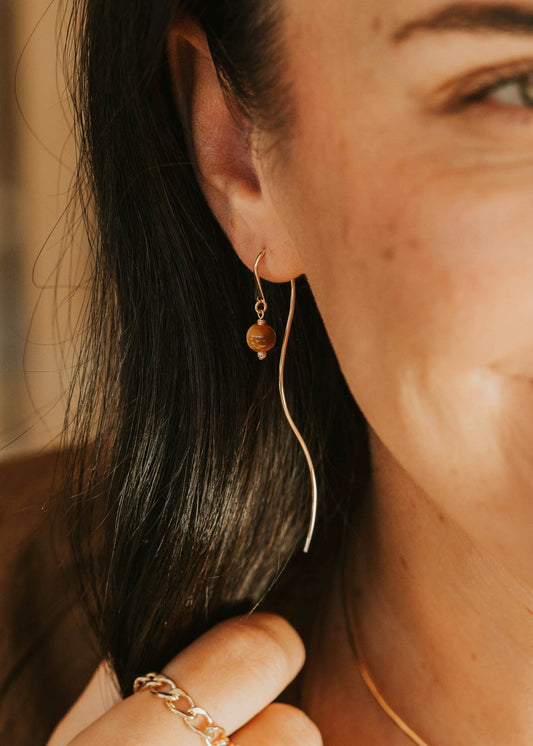 Close-up of a woman wearing gold jewelry including earrings, necklace, and ring.
