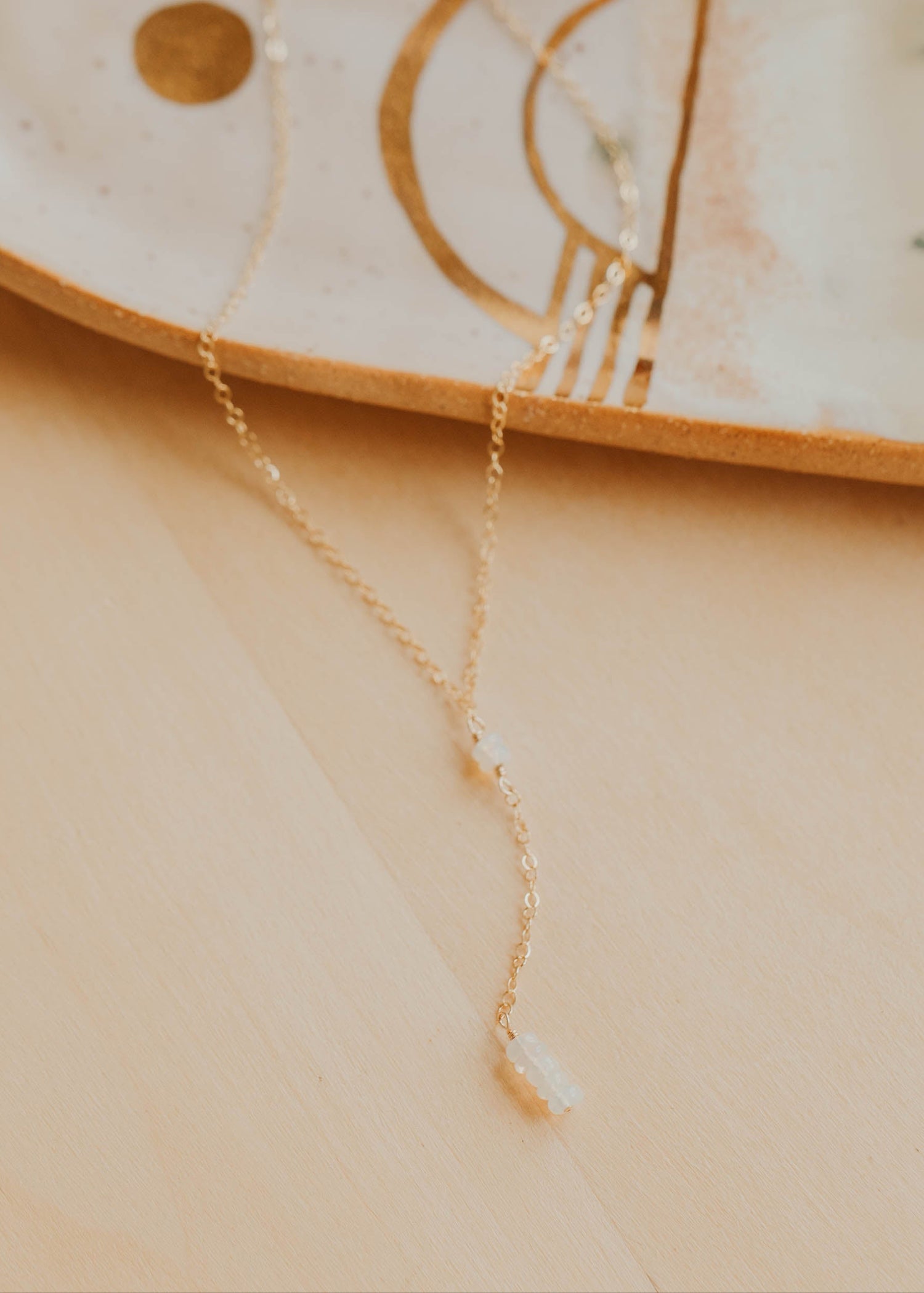 Gold necklace on a beige surface with a decorative dish in the background