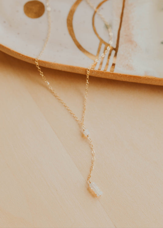 Gold necklace on a beige surface with a decorative dish in the background