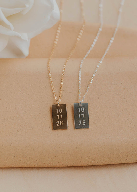 Two necklaces with rectangular pendants on a beige fabric background