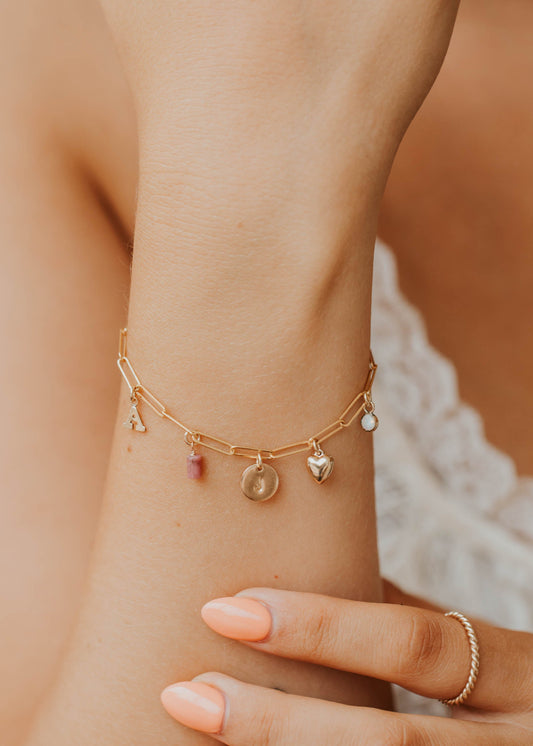 Gold bracelet with charms on a wrist against a blurred background