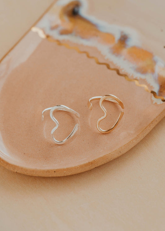 Gold and silver heart-shaped rings on a beige ceramic dish with a marble pattern.