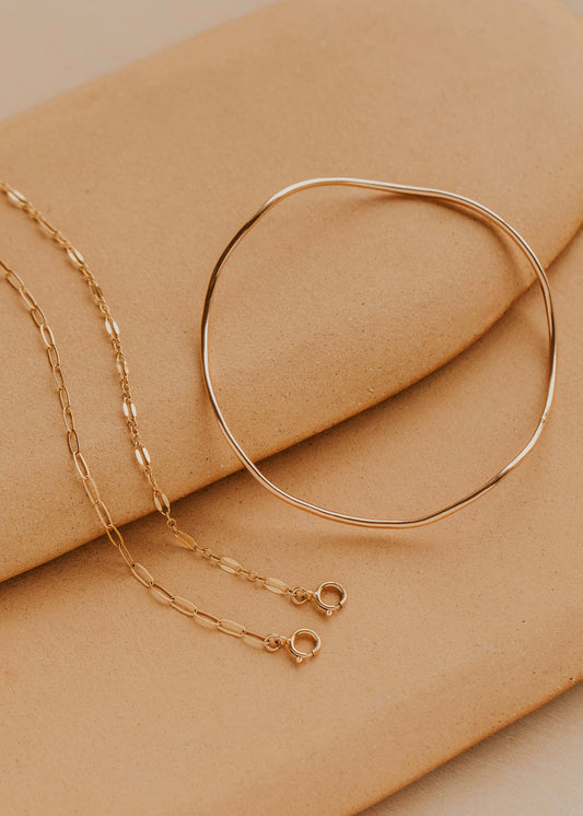Gold bracelet and chain on a beige surface