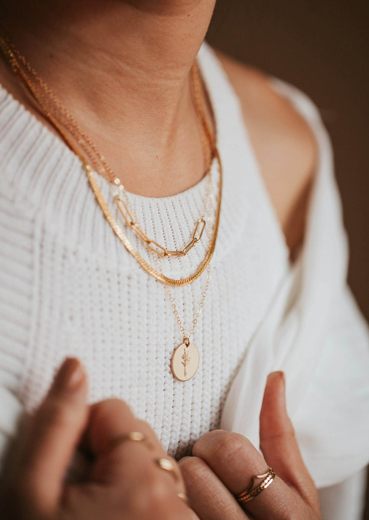 A necklace layering idea featuring a paperclip necklace linked to a dainty chain necklace paired with a necklace with flower and a thick layering chain necklace handmade by Hello Adorn.