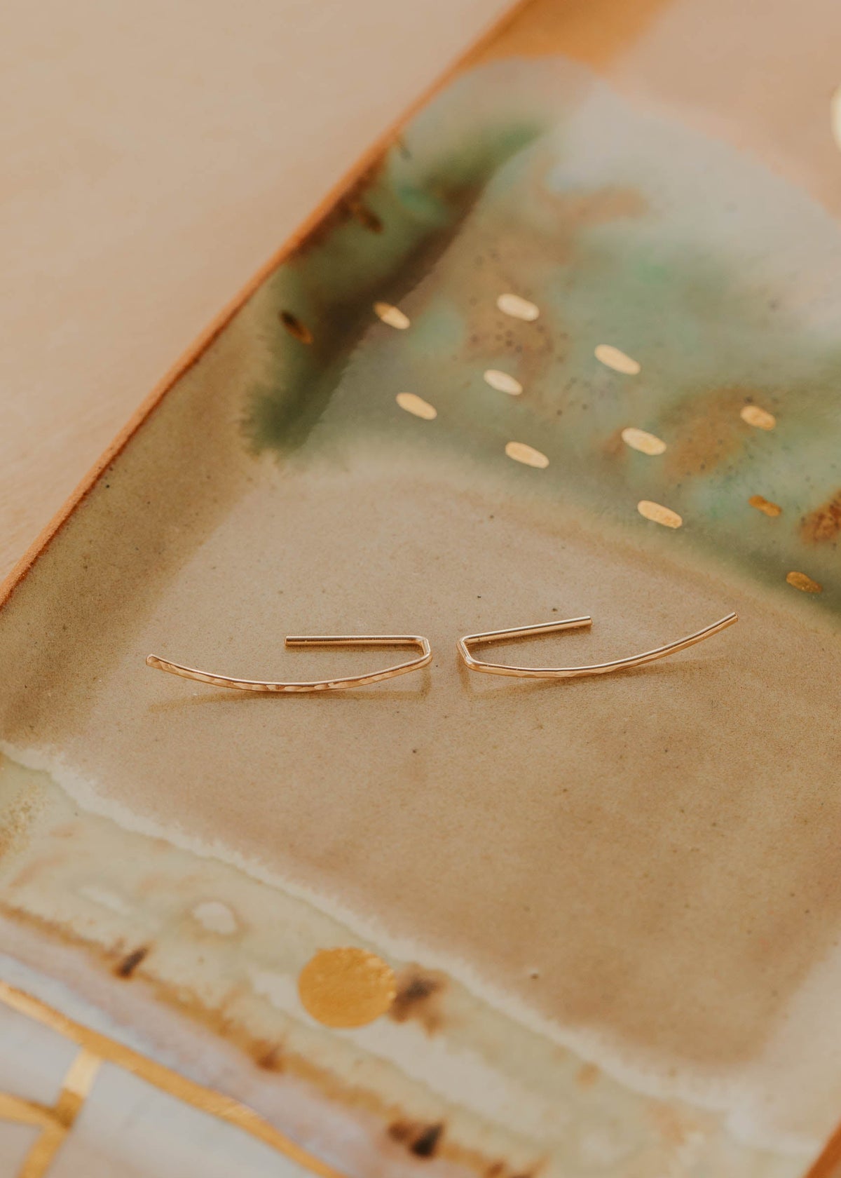 Gold earrings on a textured ceramic surface
