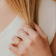 Close-up of a hand with gold rings holding blonde hair, wearing a white top.