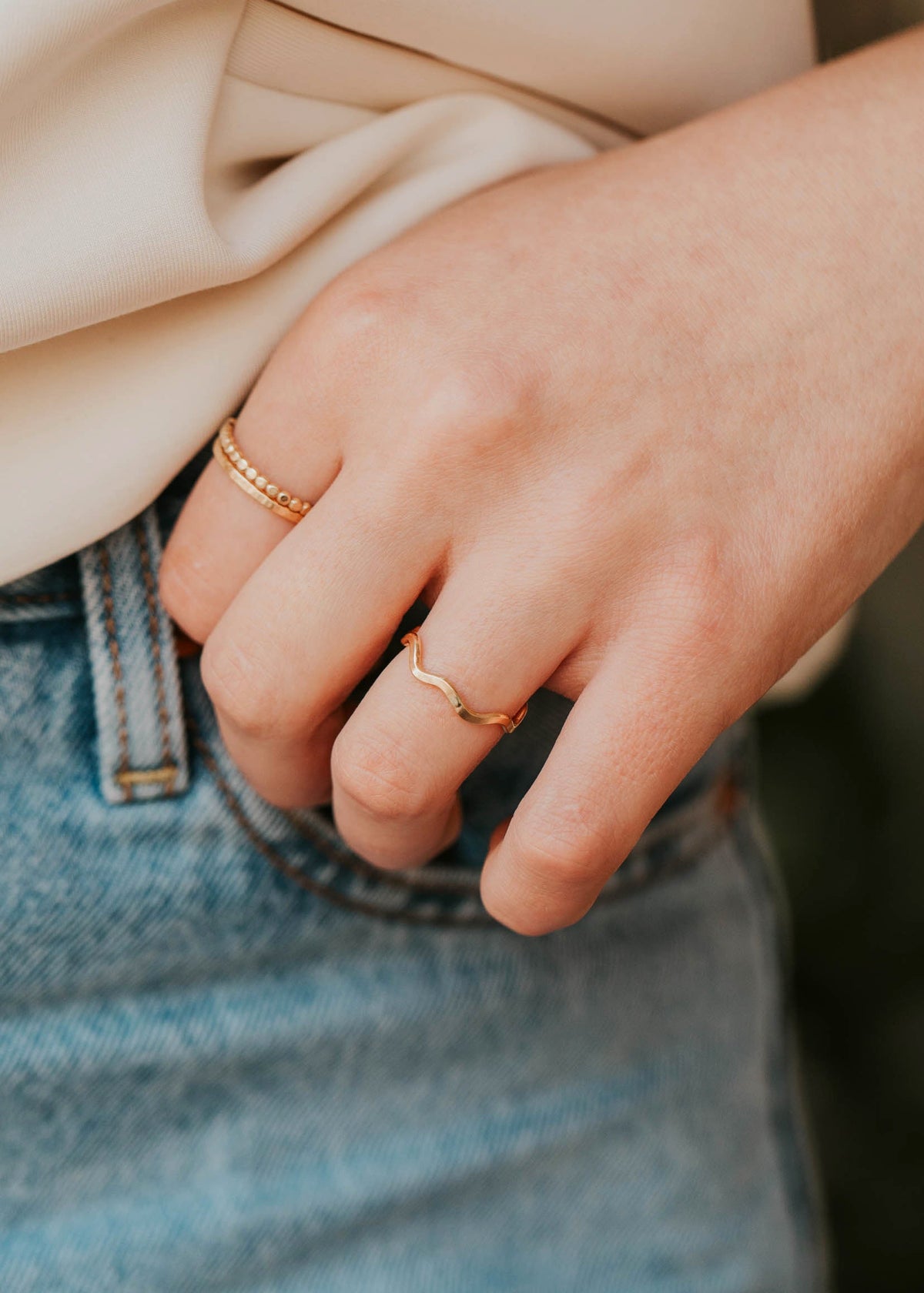 Close-up of a person wearing two gold rings on a blurred background