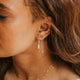 Close-up of a woman wearing gold earrings and necklaces with a neutral background