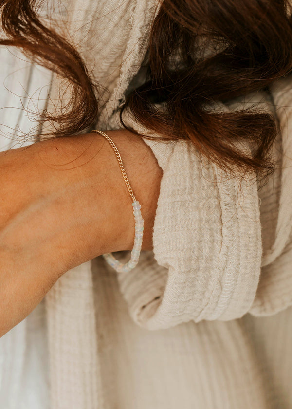 Close-up of a person wearing a beige knitted sweater and gold bracelet.