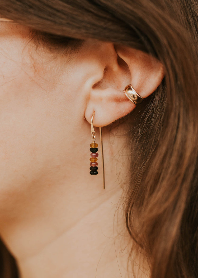 Close-up of an ear wearing a small hoop earring with colorful beads.