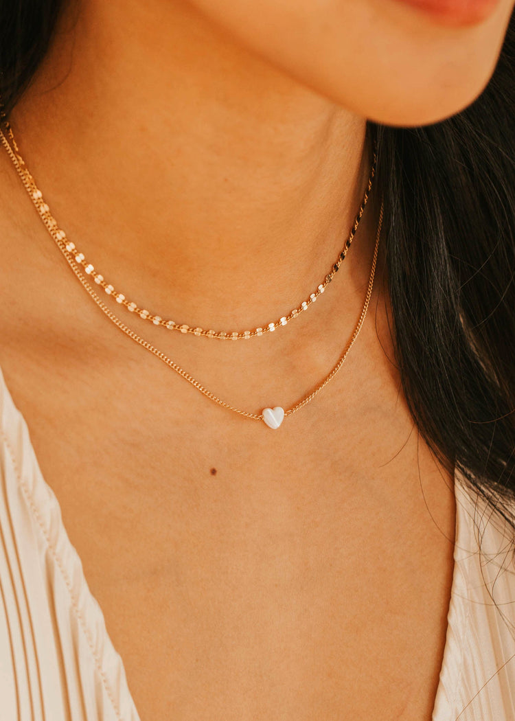 Close-up of a person wearing gold necklaces with a heart pendant.