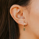 Close-up of an ear wearing a gold hoop earring with a green gemstone.
