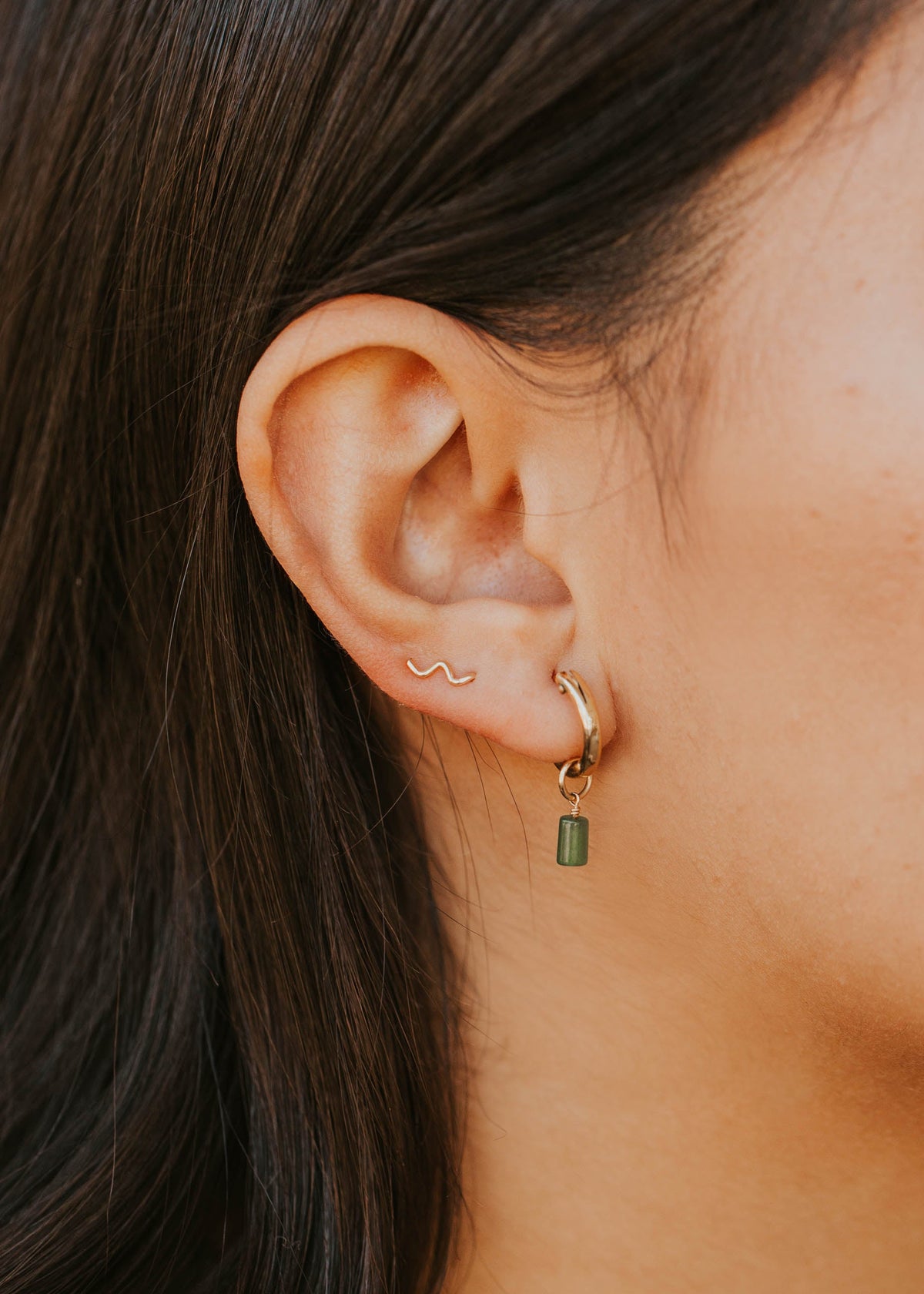 Close-up of an ear with gold and green earrings against a blurred background