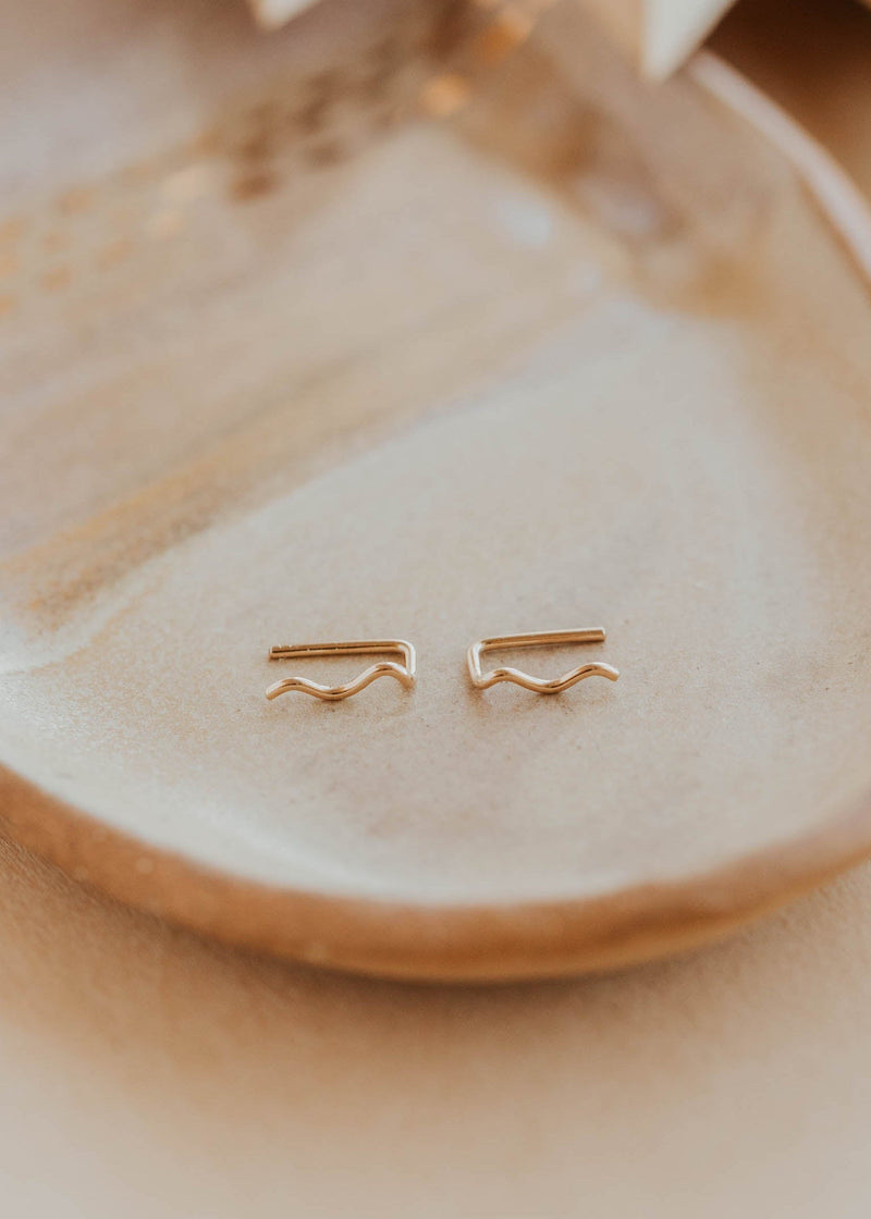 14k gold fill Tiny Wave Ear Climber earrings by Hello Adorn on a beige ceramic dish