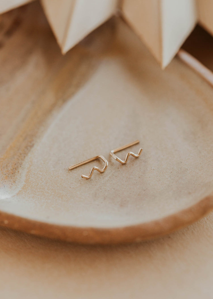 Gold earrings on a ceramic dish with a blurred background