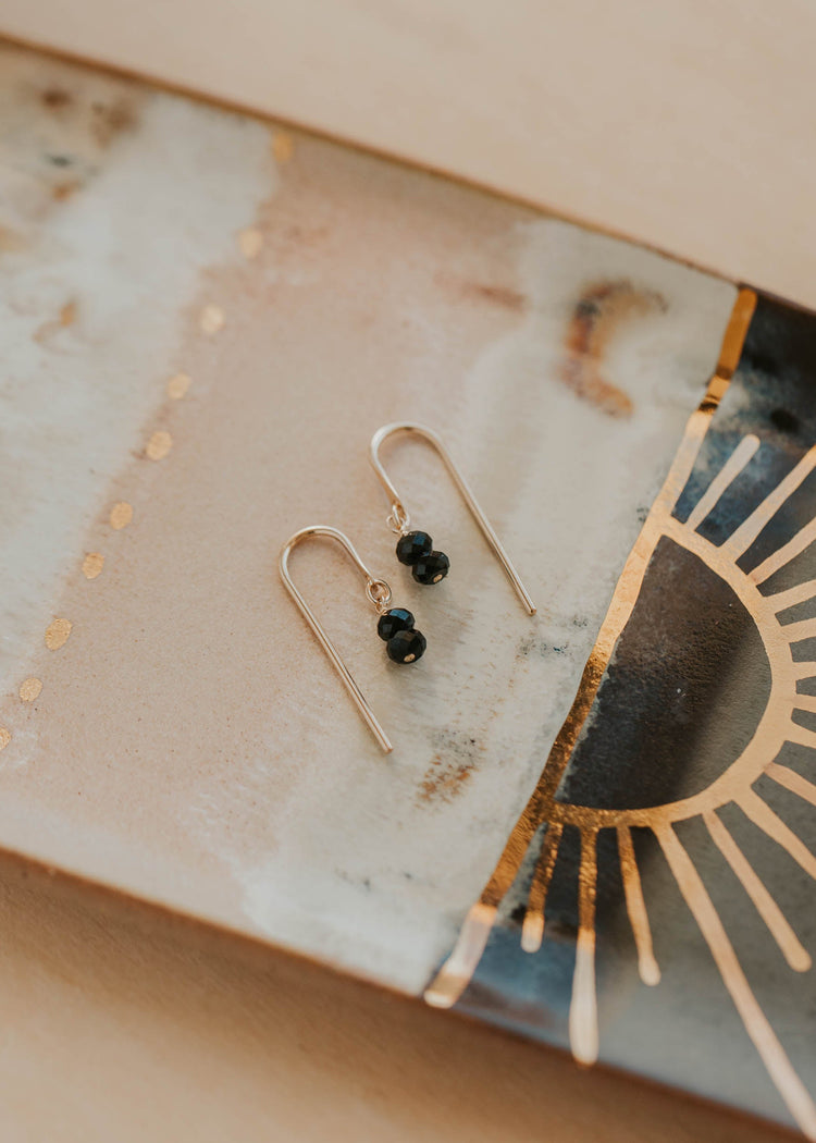Gold earrings with black beads on a decorative stone surface