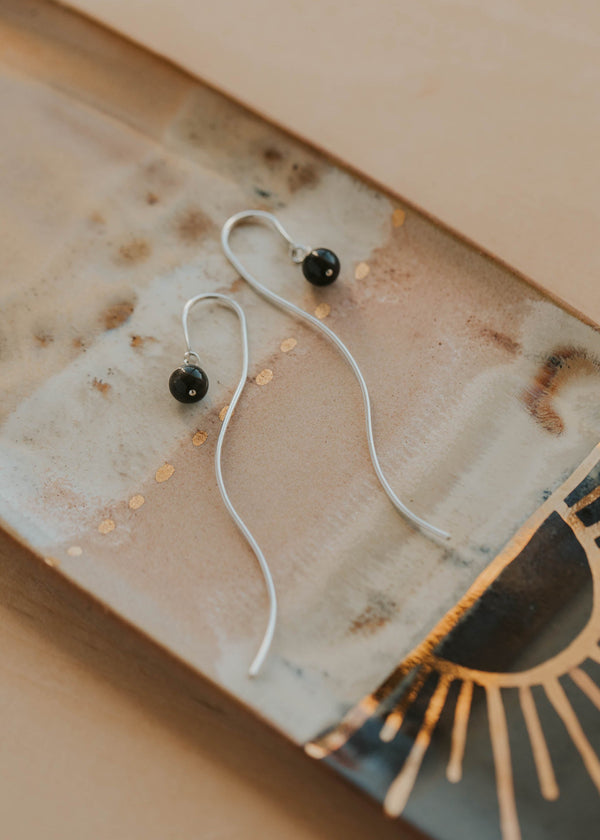 Silver earrings with black stones on a textured surface