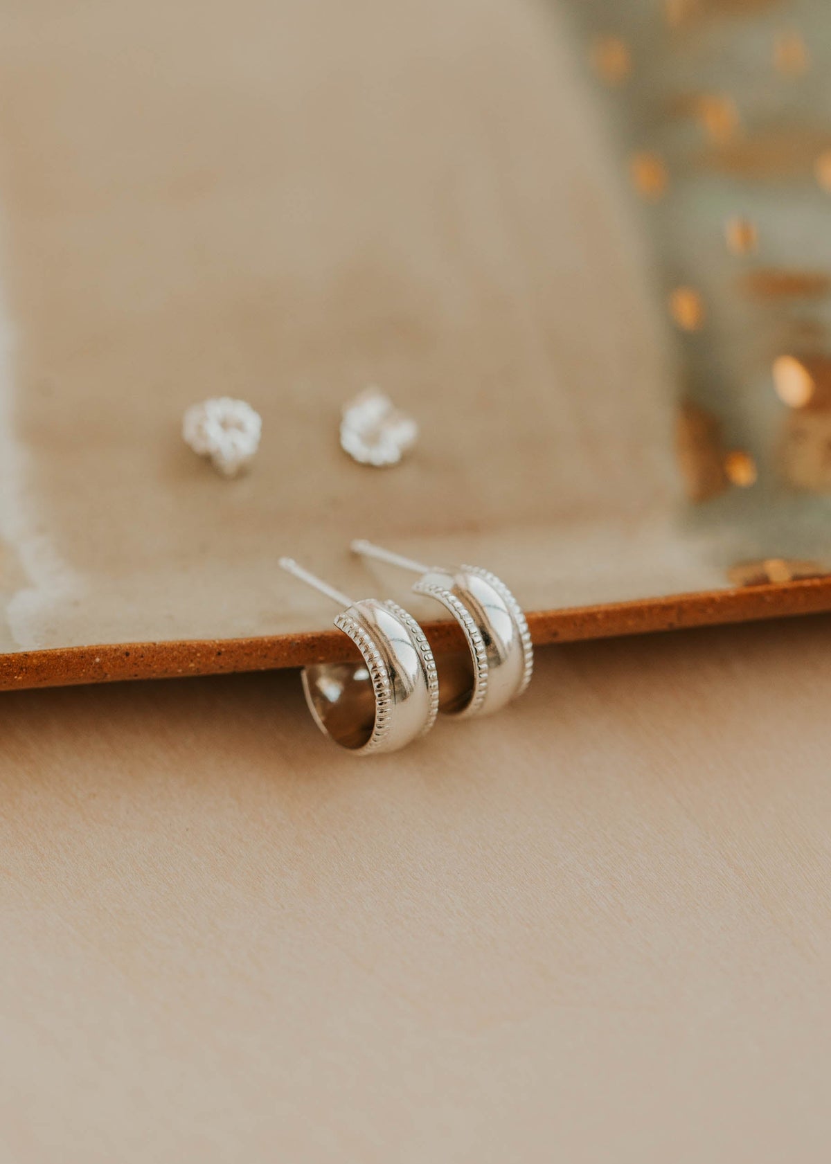 Pair of silver earrings on a beige surface with a blurred background