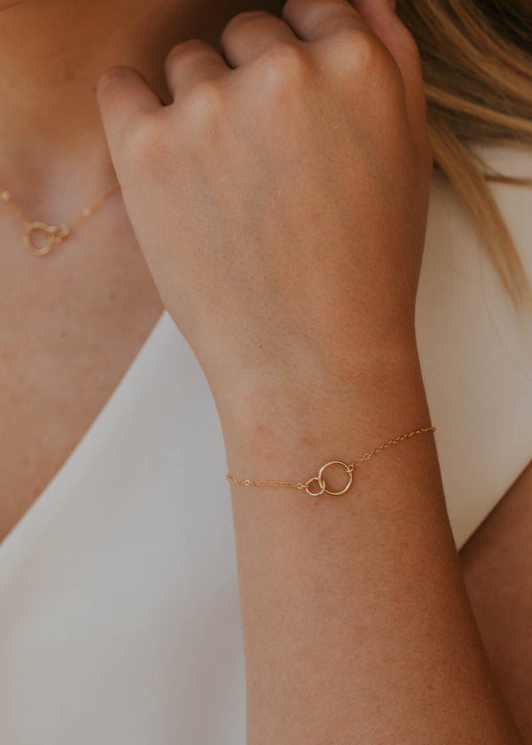 Close-up of a person's wrist wearing a gold bracelet with a minimal background