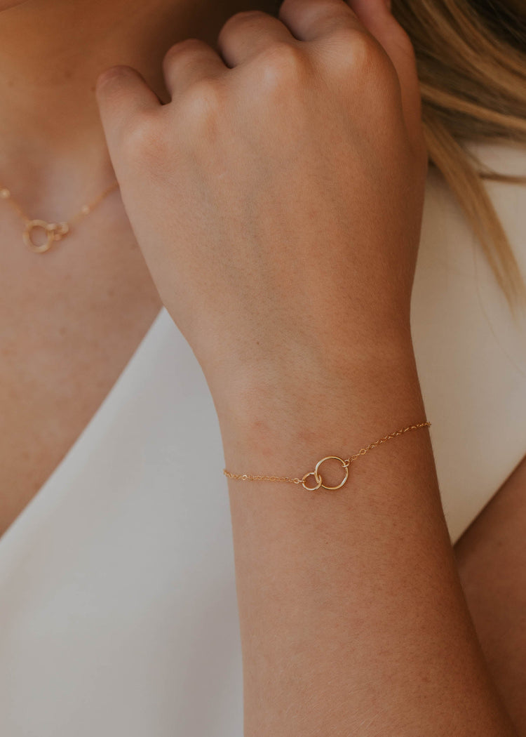Close-up of a person's wrist wearing a gold bracelet with a minimal background