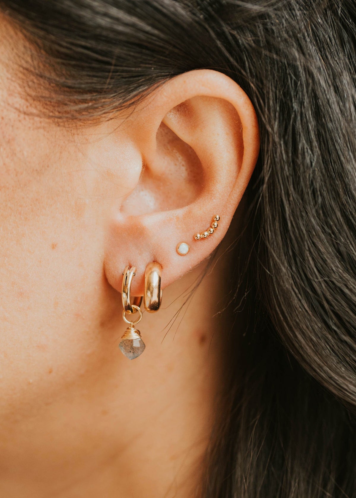 Close-up of an ear wearing gold hoop earrings with small gemstones.