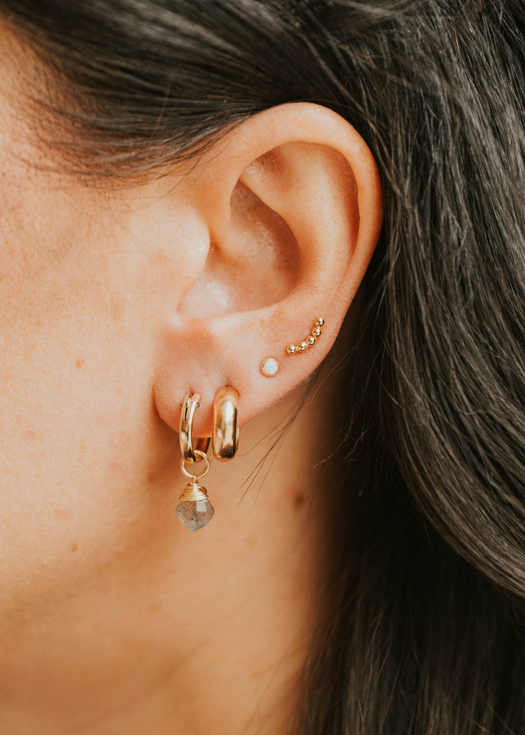 Close-up of an ear wearing gold hoop earrings with small gemstones.