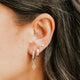 Close-up of an ear with multiple earrings and dark hair.