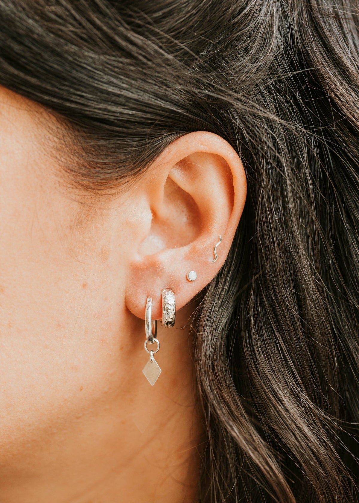 Close-up of an ear with multiple earrings and dark hair.