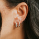 Close-up of an ear with multiple silver hoop earrings against a blurred background