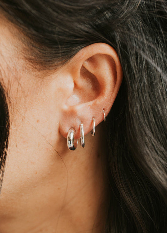 Close-up of an ear with multiple silver hoop earrings against a blurred background