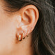 Close-up of an ear wearing gold hoop earrings with dark hair.