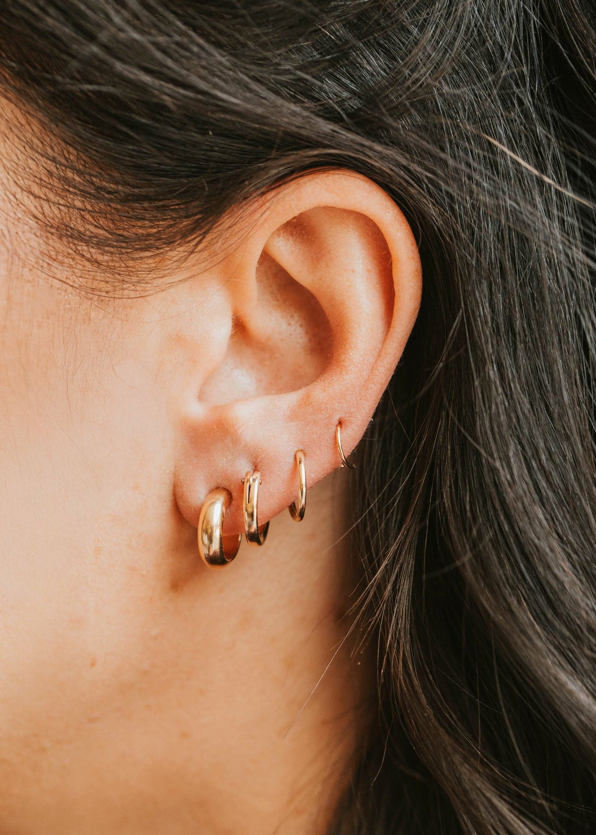 Close-up of an ear wearing gold hoop earrings with dark hair.