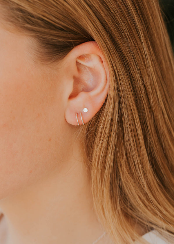 Close-up of an ear with a silver earring and blonde hair.