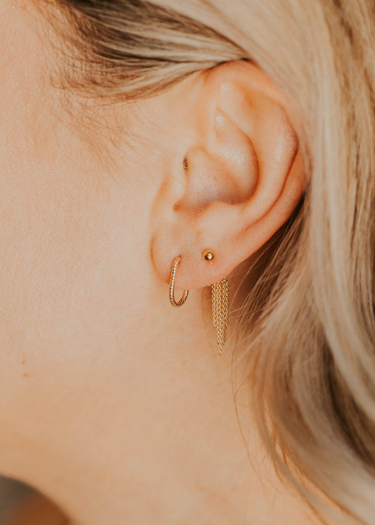 Close-up of a person's ear wearing gold earrings with blonde hair.
