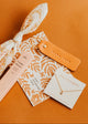 Jewelry set with floral packaging and orange tag on a brown background