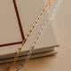 Gold and silver chain necklaces on a beige surface with a book in the background