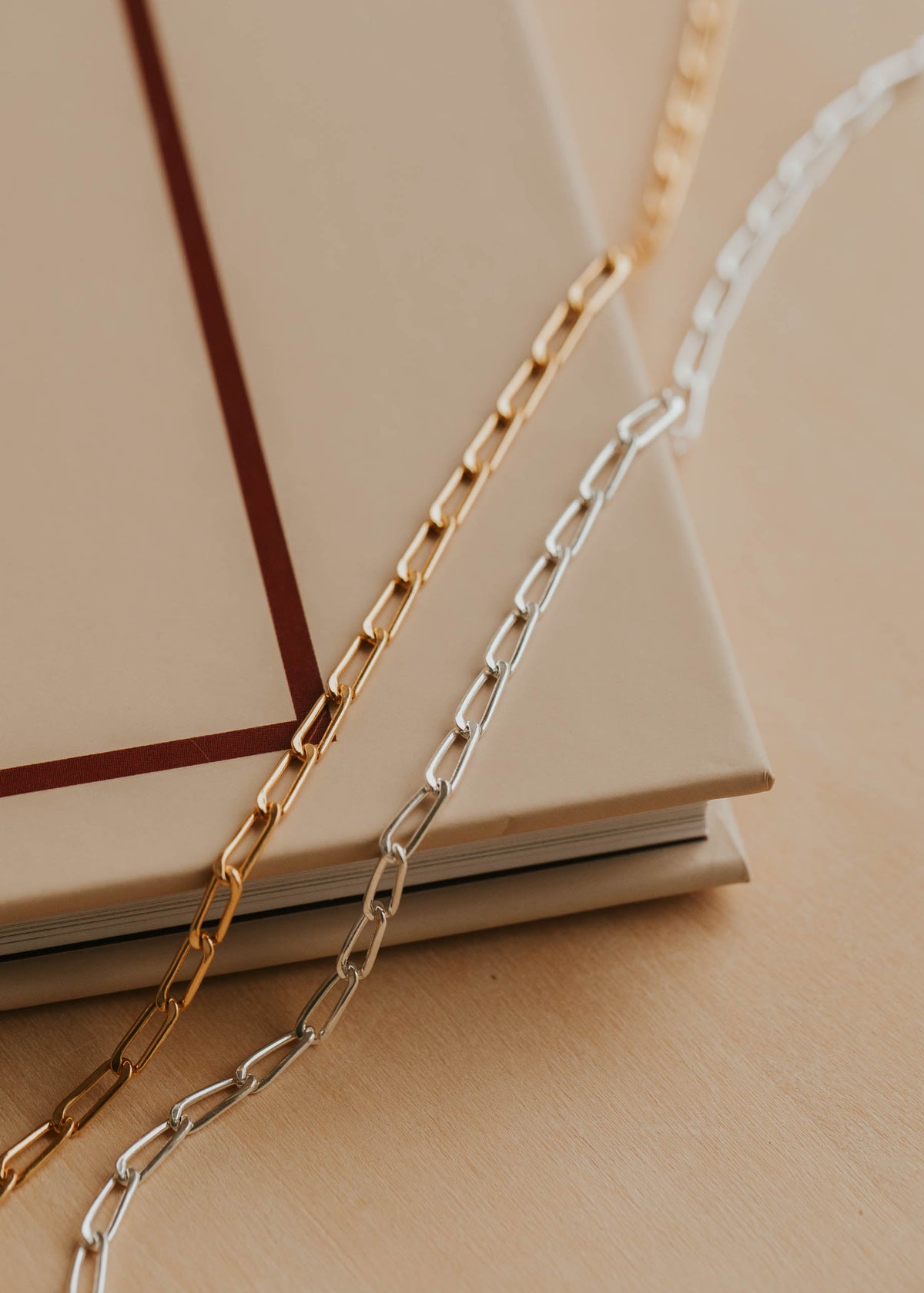 Gold and silver chain necklaces on a beige surface with a book in the background