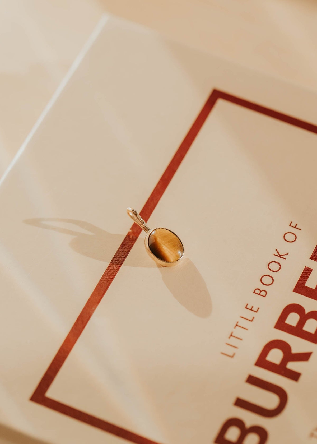 Gold tigers eye pendant sitting on a Burberry book