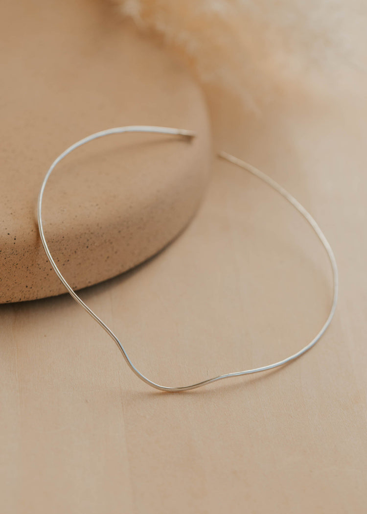 Silver necklace cuff on a beige stone surface