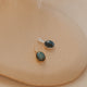 Pair of pendants with green gemstones on a beige surface