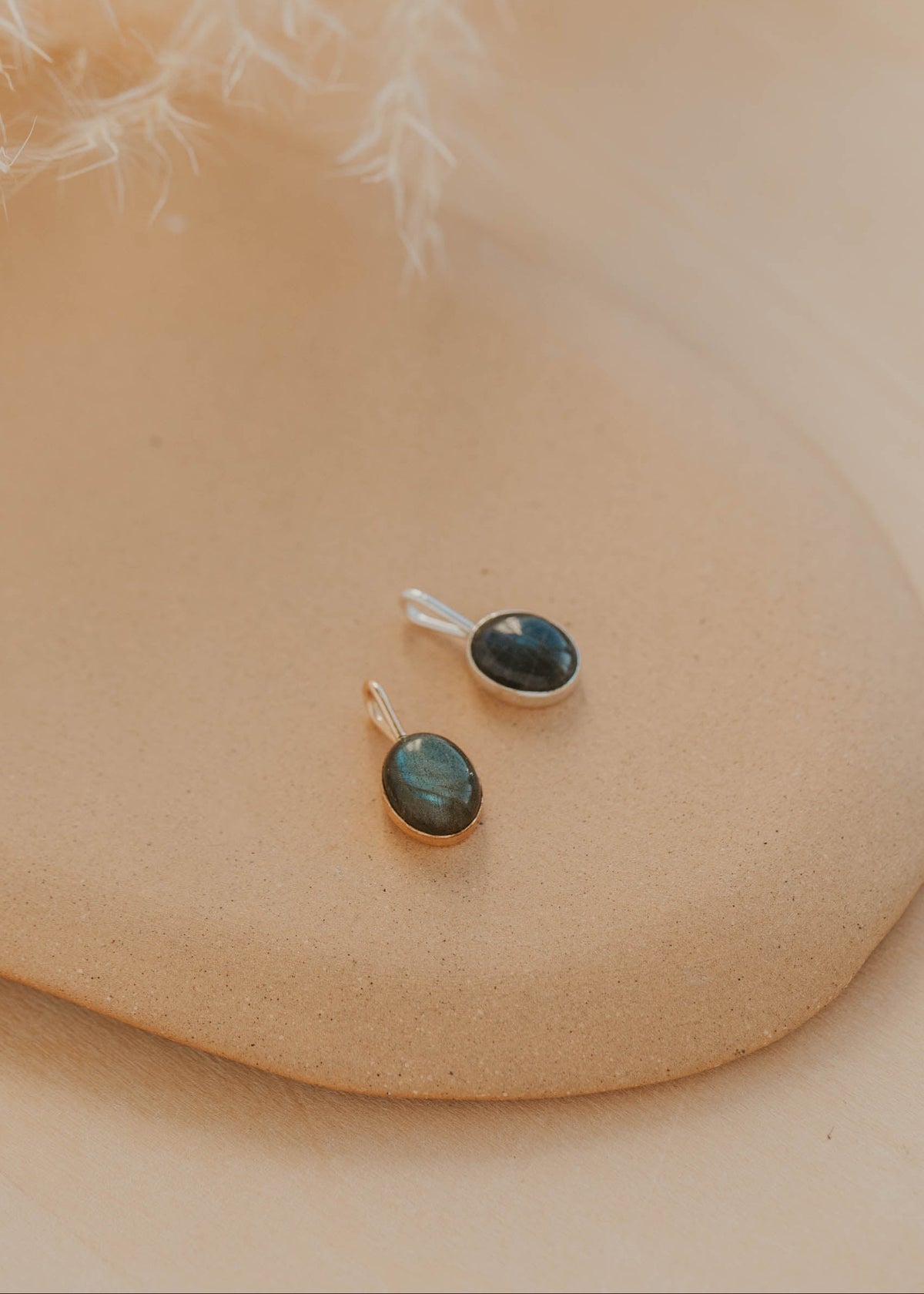 Pair of pendants with green gemstones on a beige surface