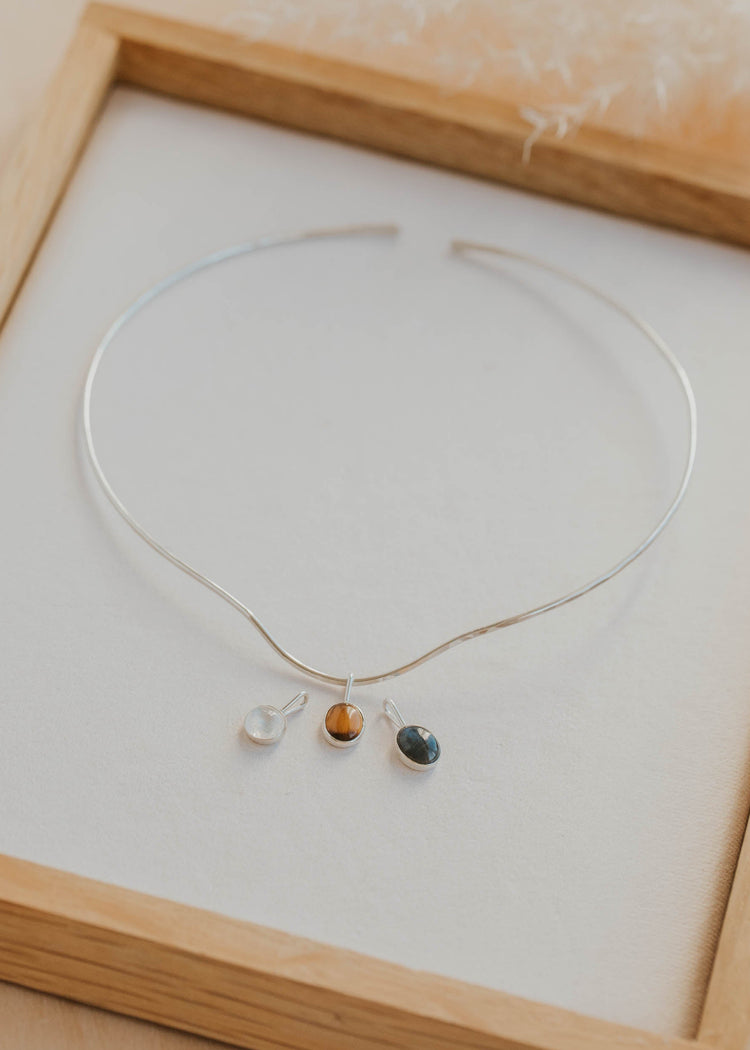 Silver necklace with three small colored stones in a wooden frame