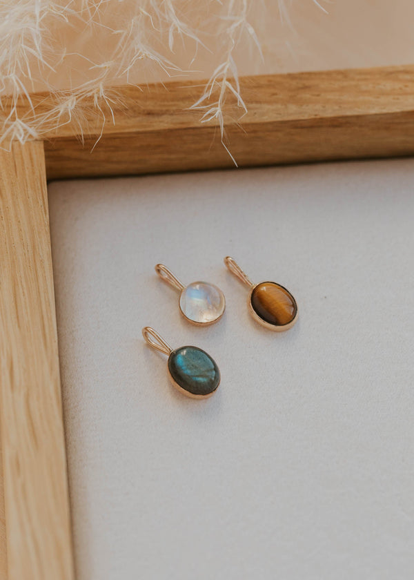 Three gold pendant necklaces with gemstones on a white surface with a wooden frame.